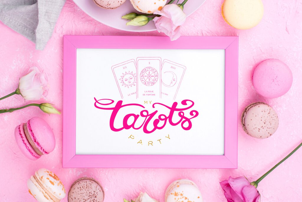 A pink-framed sign reading My Tarots Party with tarot cards is surrounded by pink and yellow macarons and pale flowers on a pi