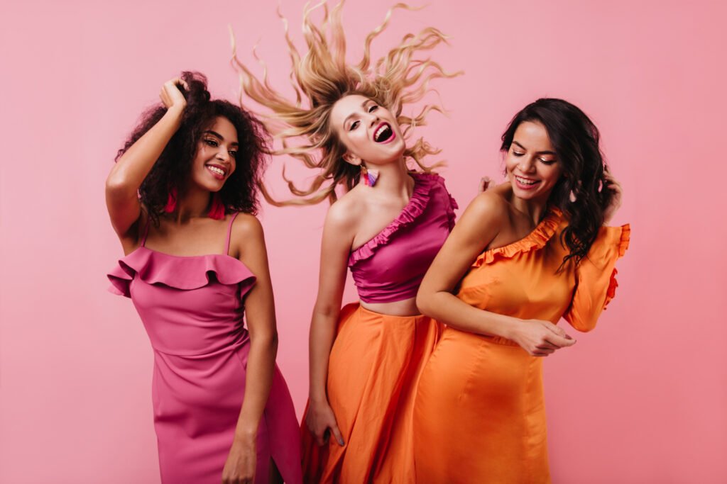 Blonde girl funny dancing in studio. Glamorous latin woman posing in orange dress.