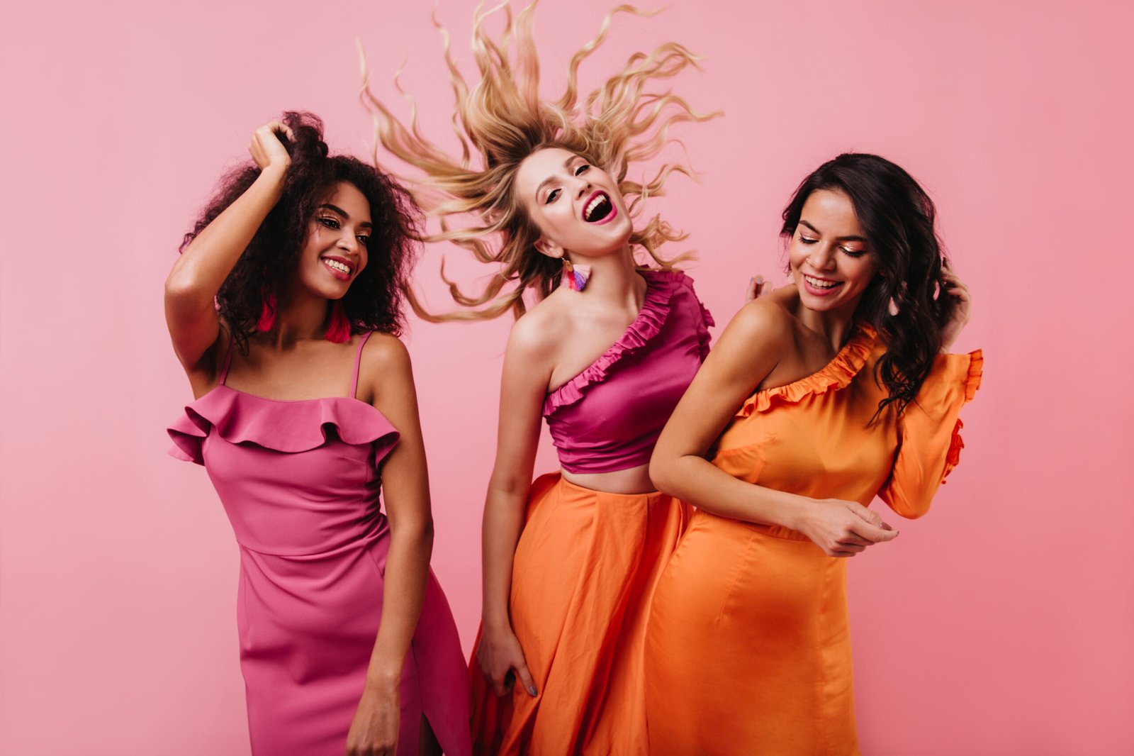 Blonde girl funny dancing in studio. Glamorous latin woman posing in orange dress.