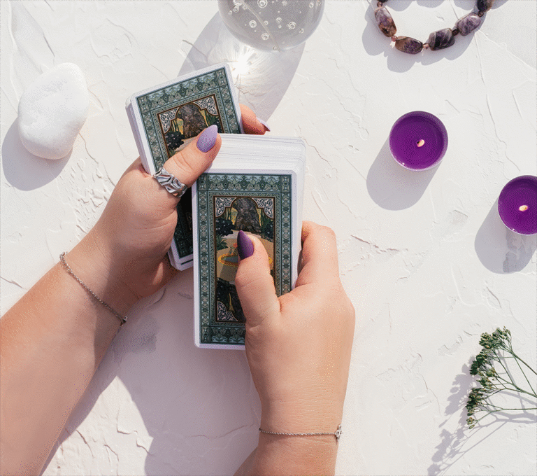 two hands holding tarots cards on a white table with a white stone, two purple candles.